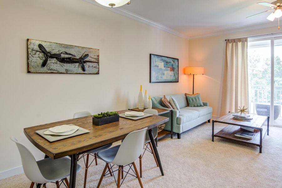 Modern living and dining area with wood table, light sofa, wall art, and large window with curtains.