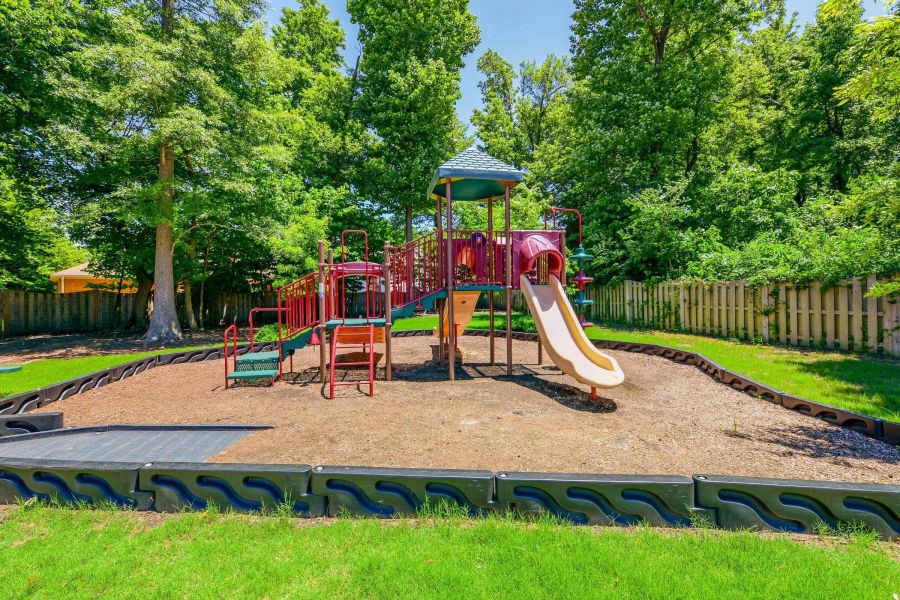 Colorful playground with slides and climbing structures surrounded by trees and a grassy area on a sunny day.
