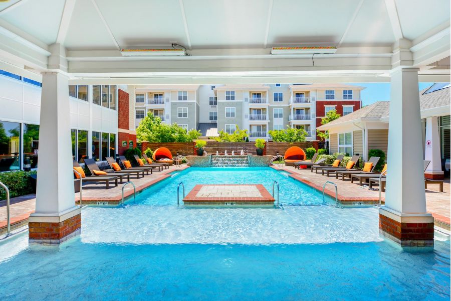 Resort-style outdoor pool area with lounge chairs, cabanas, and modern apartment buildings in the background.