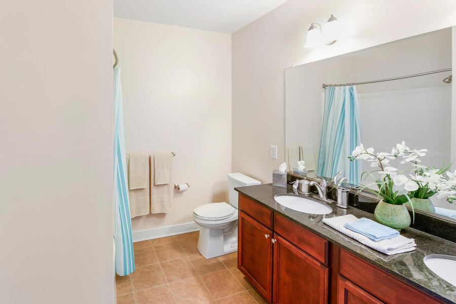 Modern bathroom with a double sink, toilet, shower, mirror, towels, and flowers on the counter.