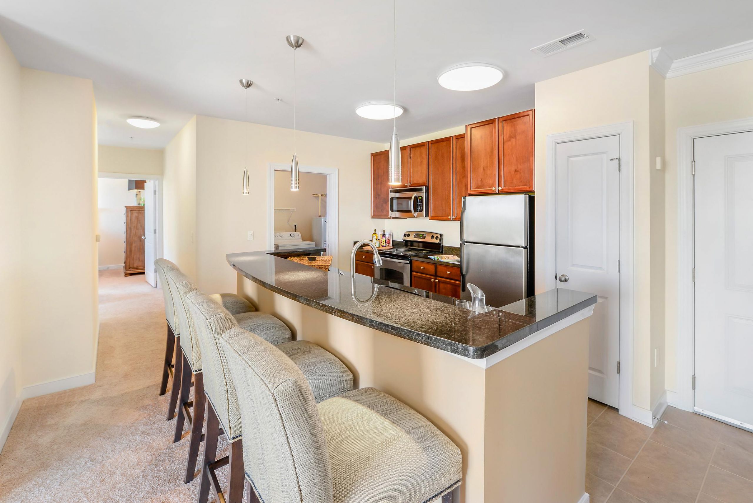 Modern kitchen with a granite island, barstools, stainless steel appliances, and wooden cabinets.