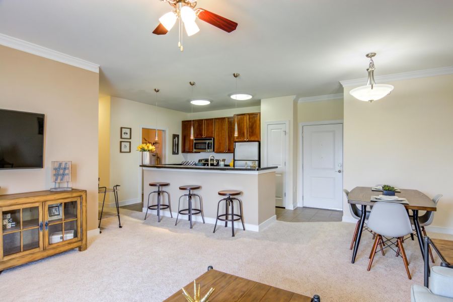 Modern open-plan living area with kitchen, bar stools, dining table, and neutral-colored decor.