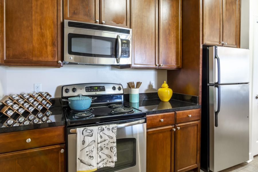 Modern kitchen with stainless steel appliances, wooden cabinets, and a yellow jar on the black countertop.