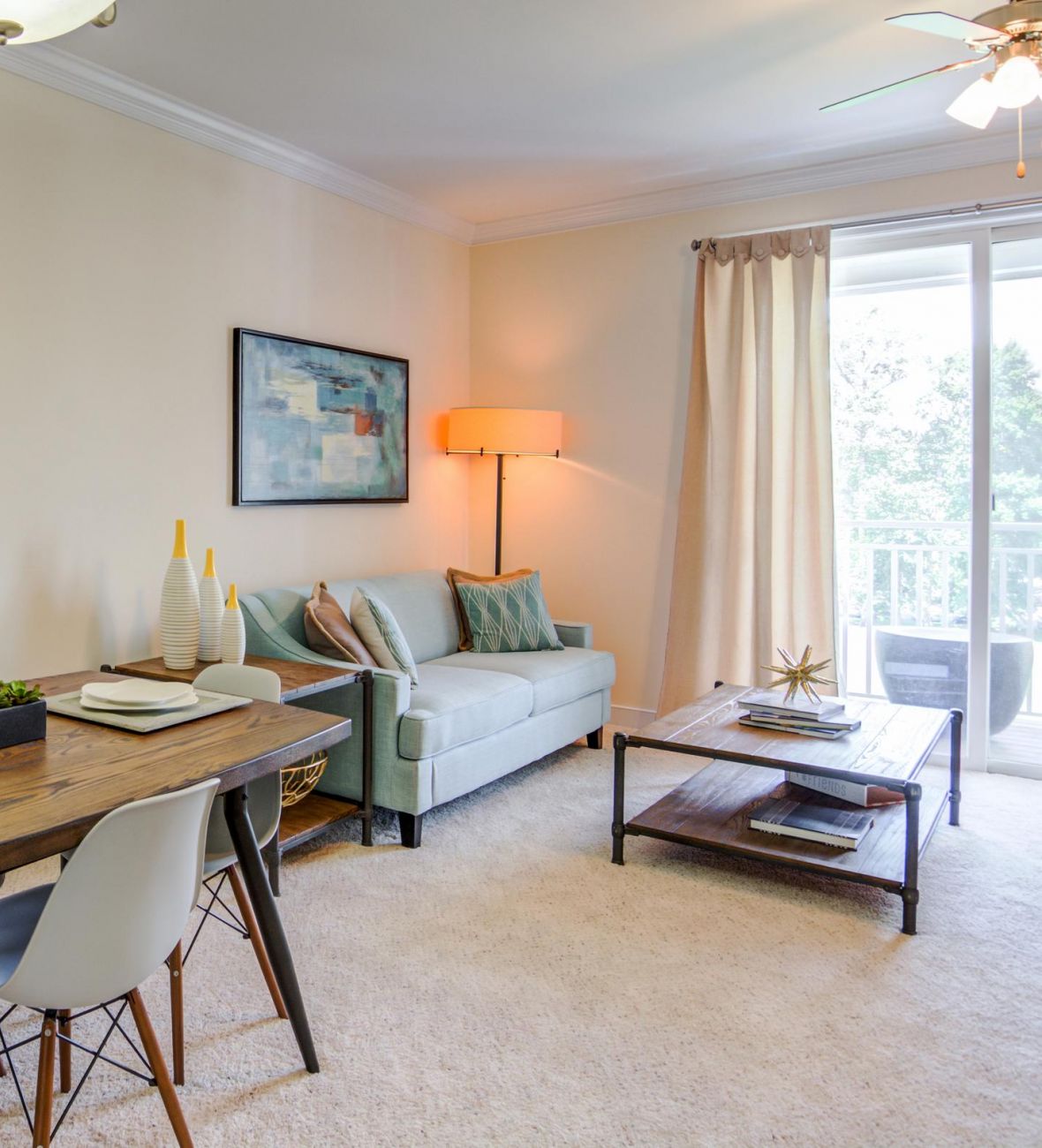 Modern living and dining area with wood table, light sofa, wall art, and large window with curtains.