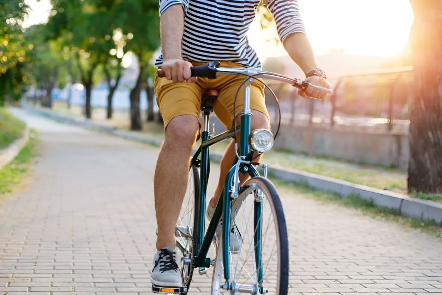 Person wearing a striped shirt and yellow shorts riding a bicycle on a sunlit park path.