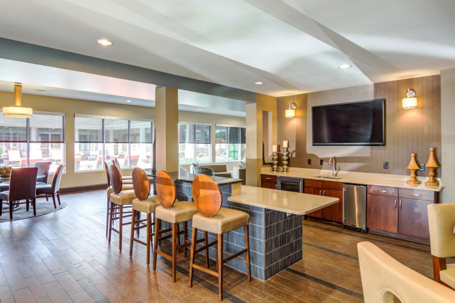 Modern communal kitchen and lounge area with bar seating, large windows, and a TV on the wall.