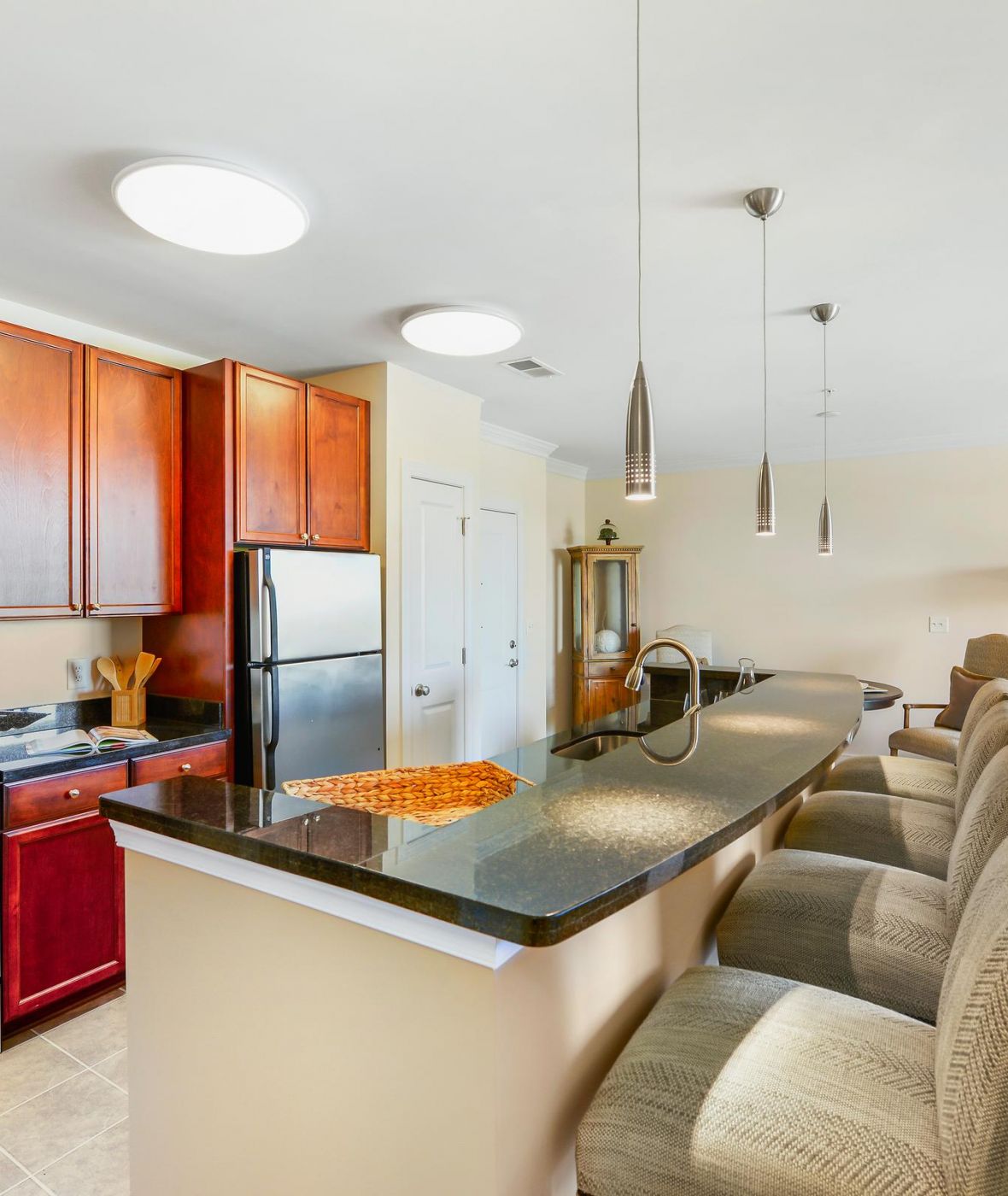 Modern kitchen with stainless steel appliances, wood cabinets, and a breakfast bar with four upholstered chairs.