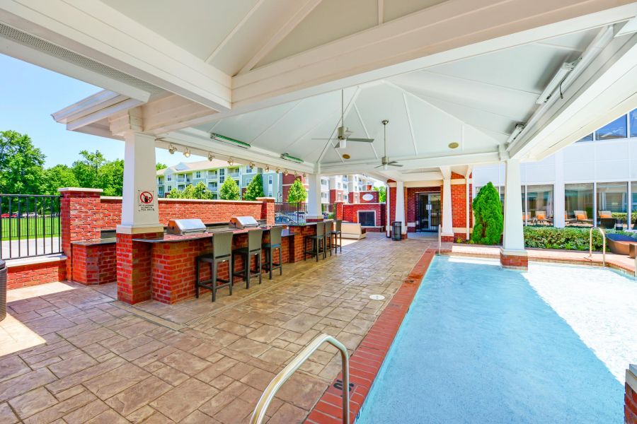 Covered outdoor kitchen and bar area beside a shallow pool with seating and ceiling fans.
