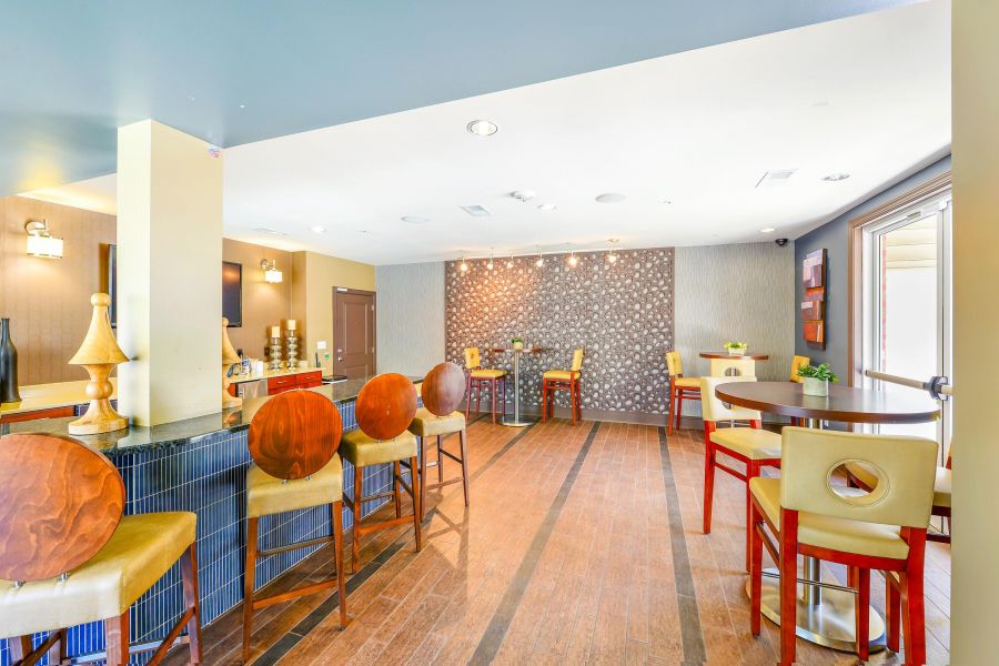 Modern lounge with wooden chairs, round tables, and patterned accent wall, brightly lit by natural light.