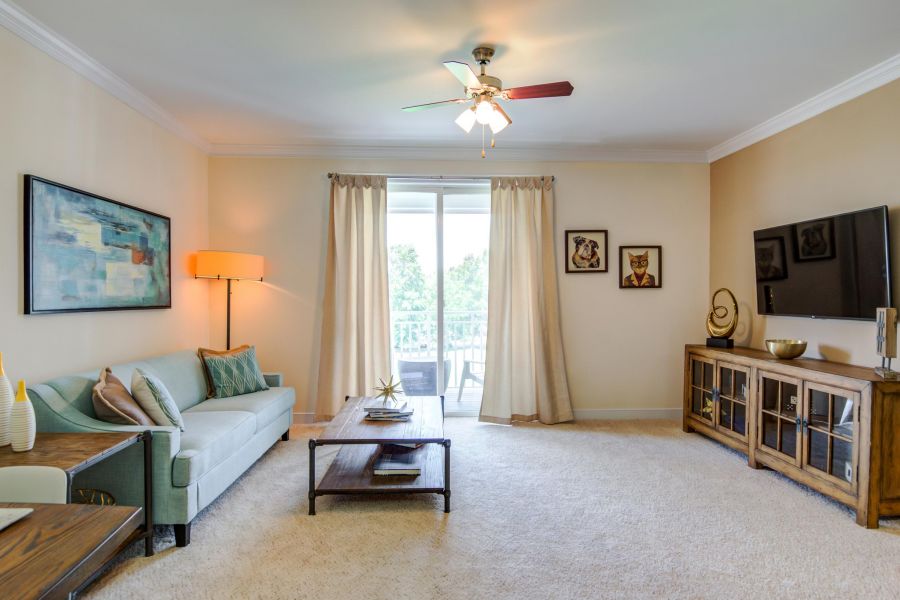 Bright living room with a sofa, coffee table, TV, art on the walls, and glass doors leading to a balcony.