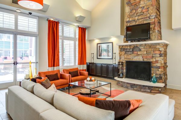 Modern living room with stone fireplace, orange accents, large windows, and a beige sectional sofa.