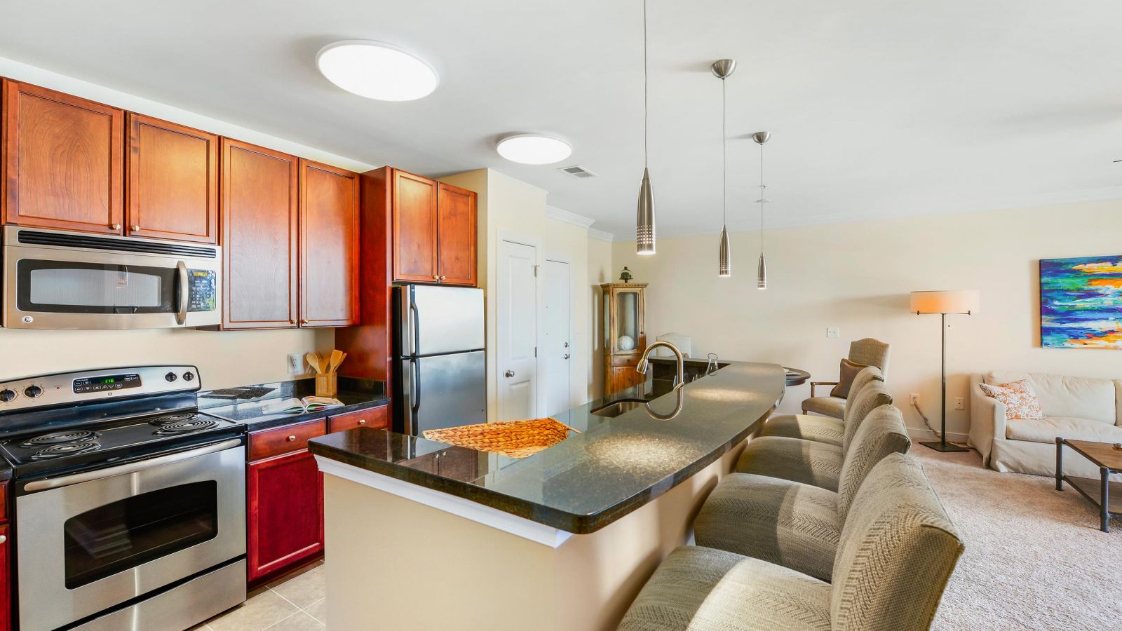 Modern kitchen with stainless steel appliances, wood cabinets, and a breakfast bar with four upholstered chairs.