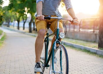 Person wearing a striped shirt and yellow shorts riding a bicycle on a sunlit park path.