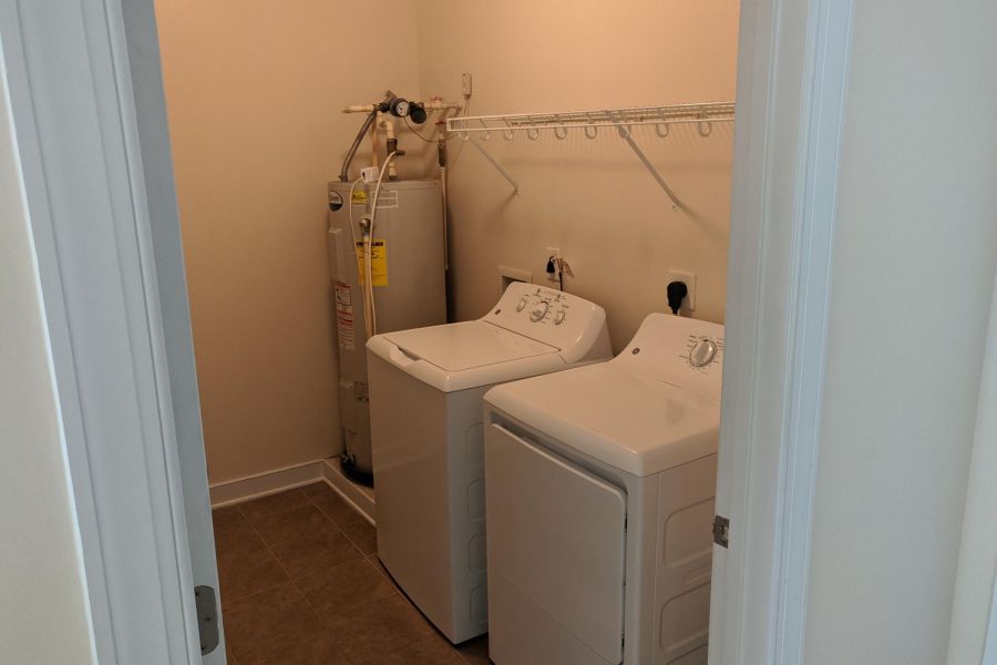 Laundry room with a washer, dryer, water heater, tile floor, and a wire shelf on the wall.