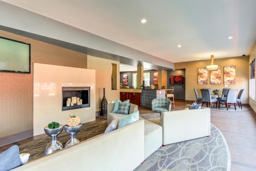 Modern lounge with cream sofas, small tables, wall art, and dining area in a well-lit, open space.